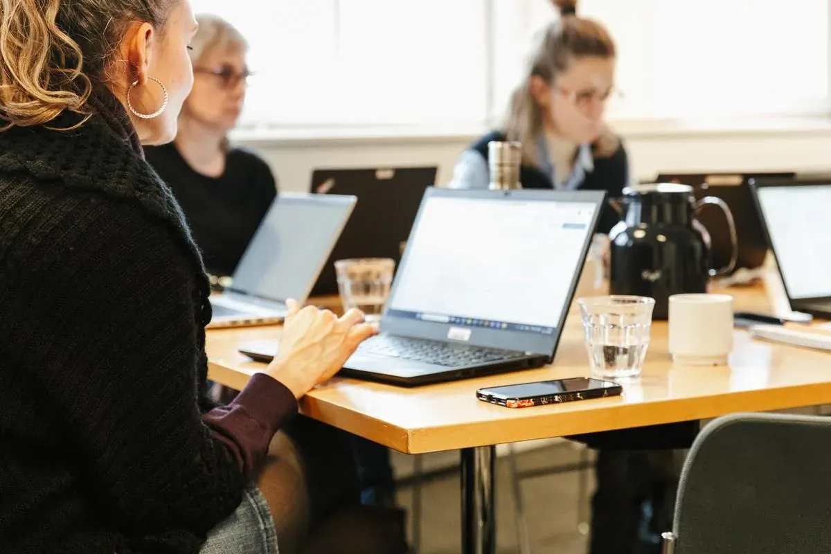 Participants work on laptops around a shared table during a course.