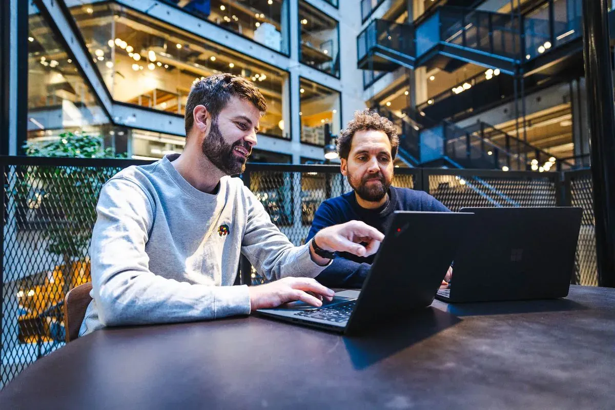 Two people look at a laptop together while one of them points at the screen.